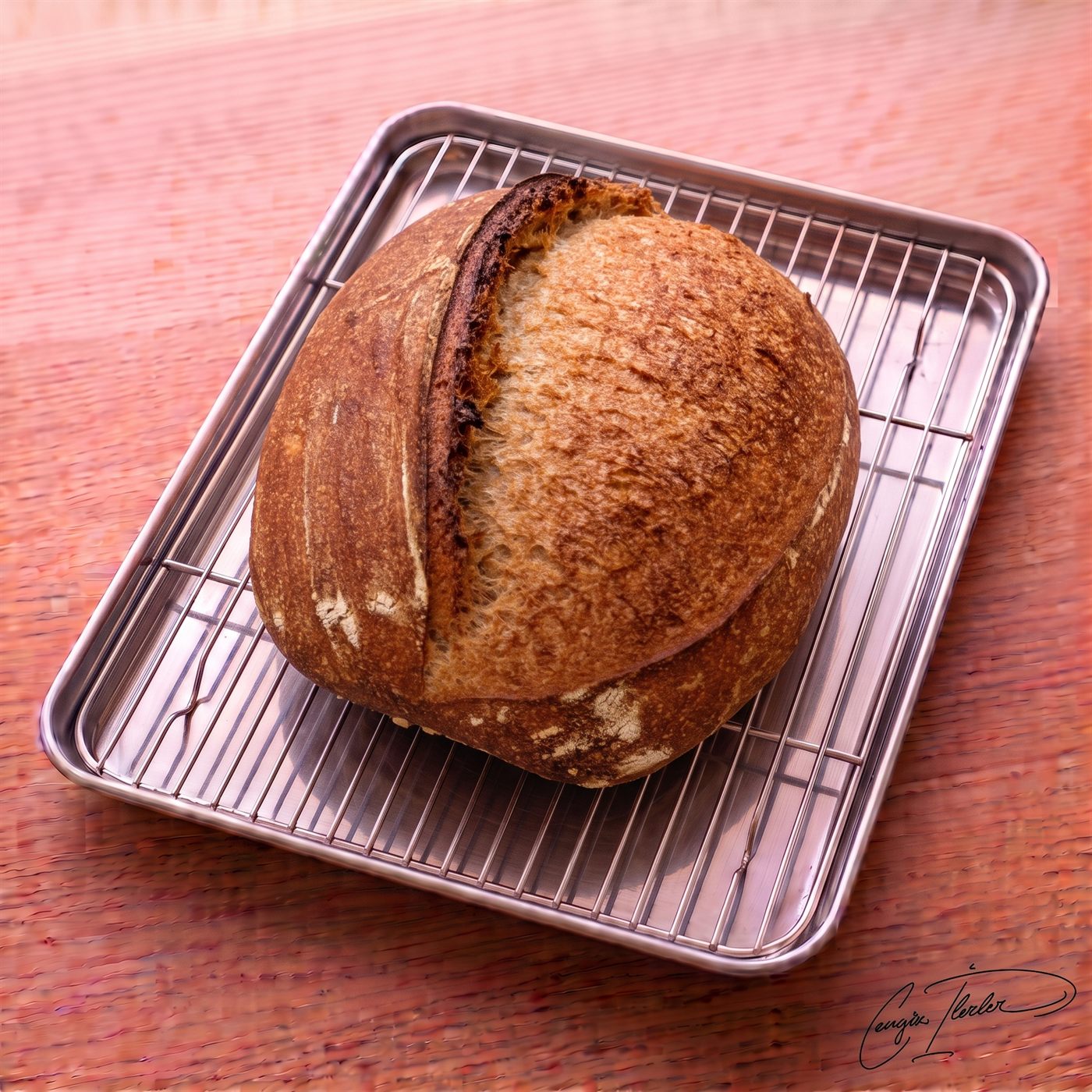 A round boule of sourdough whole wheat bread with a dark, blistered crust and a single curved scoring mark, resting on a wire cooling rack over a wooden surface.