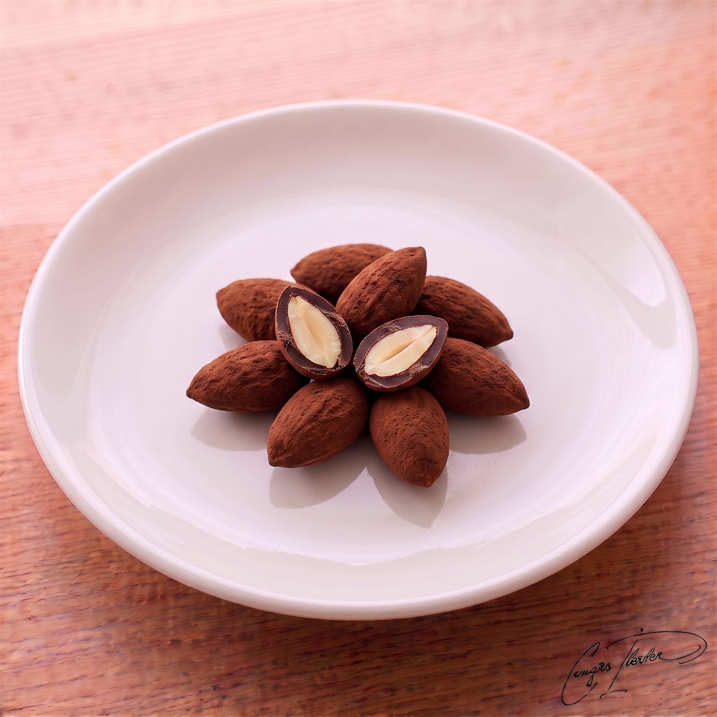 A neat flower-shaped arrangement of cocoa-dusted almond dragees on a white plate, with the center one cut open to reveal a whole roasted almond inside.