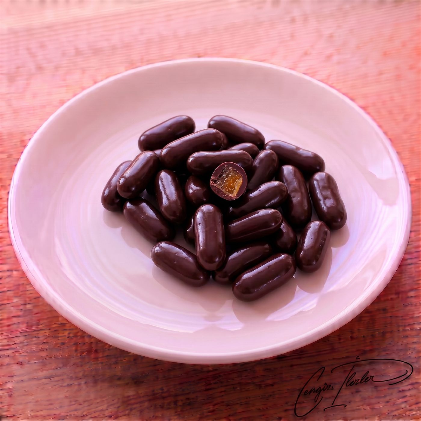 A small pile of dark chocolate-coated orange dragees on a white plate, with one piece cut open to reveal a bright orange candied center.