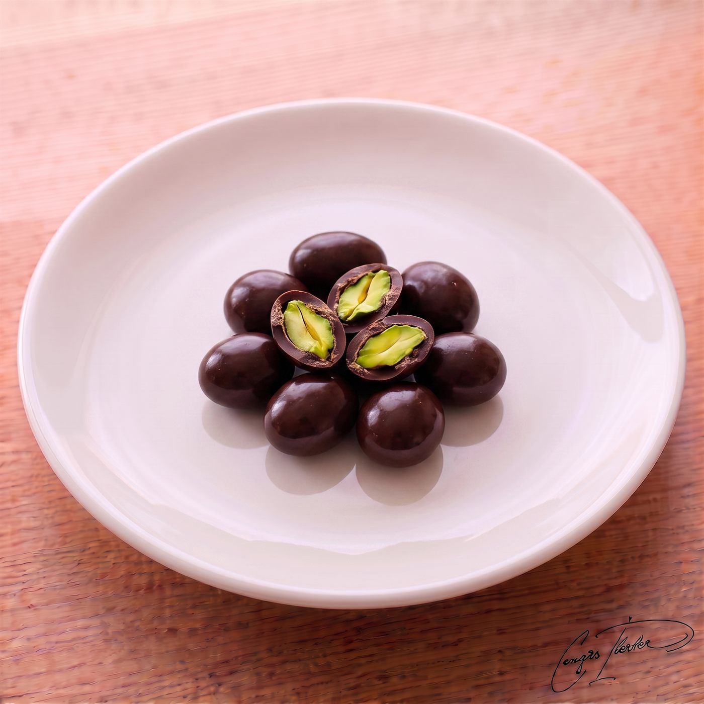 A flower-shaped arrangement of dark chocolate-coated pistachio dragees on a white plate, with the top pieces cut open to reveal bright green whole pistachios inside.