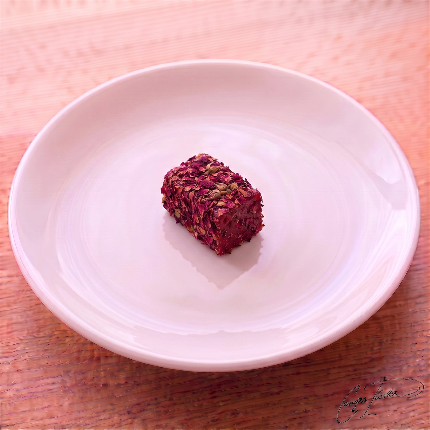 A single piece of lokum entirely coated in dried, dark pink rose petals, resting on a white plate.