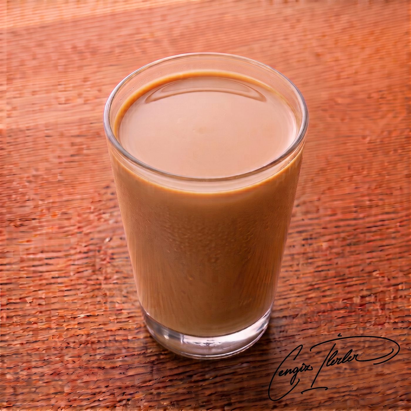A cold glass of milk mixed with carob molasses, giving it a creamy light brown color, with condensation on the outside of the glass.
