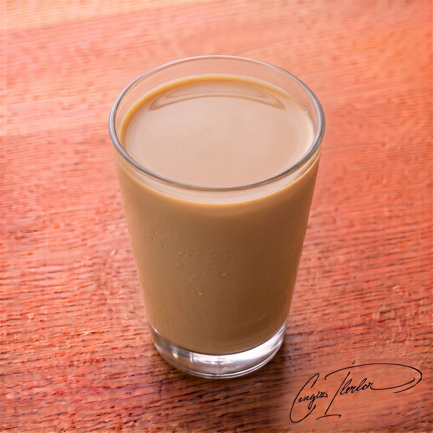 A glass of creamy, light brown milk coffee resting on a wooden surface.