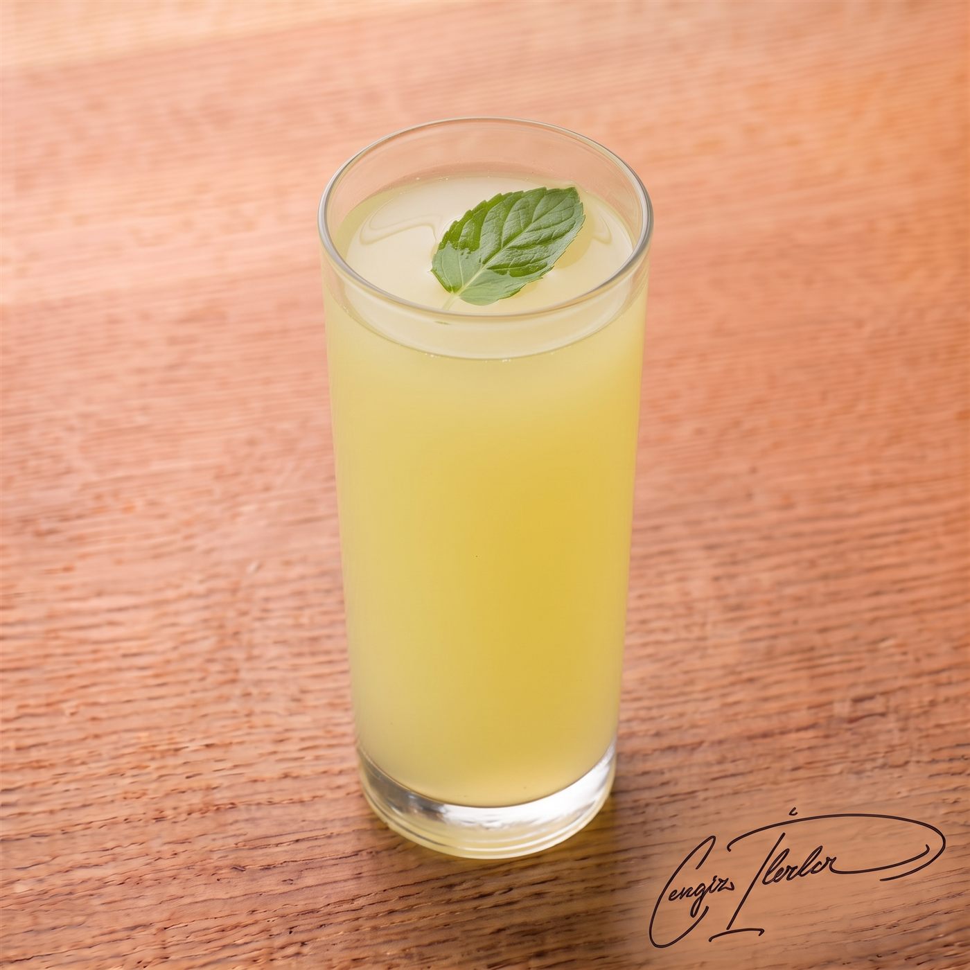 A tall glass of cloudy Turkish lemonade with a single mint leaf floating on top.