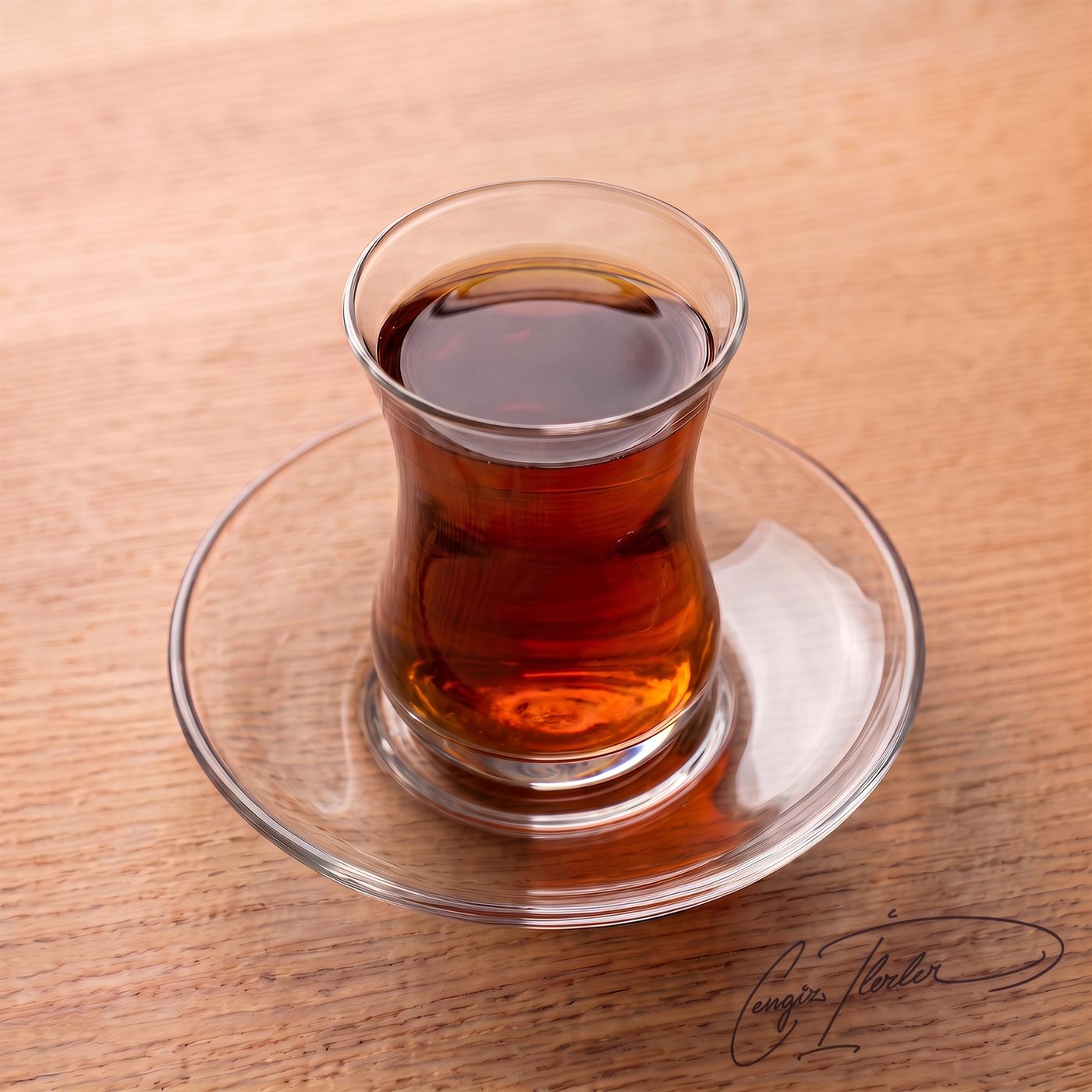 A tulip-shaped ince belli glass of dark amber Turkish tea on a glass saucer.