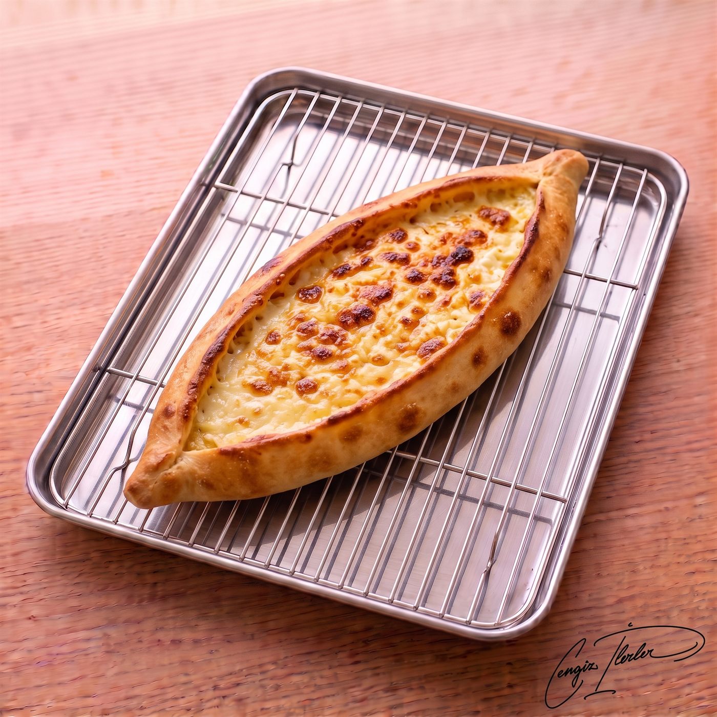 A freshly baked, boat-shaped kaşarlı pide filled with bubbling, golden-brown melted cheese, resting on a metal cooling rack.
