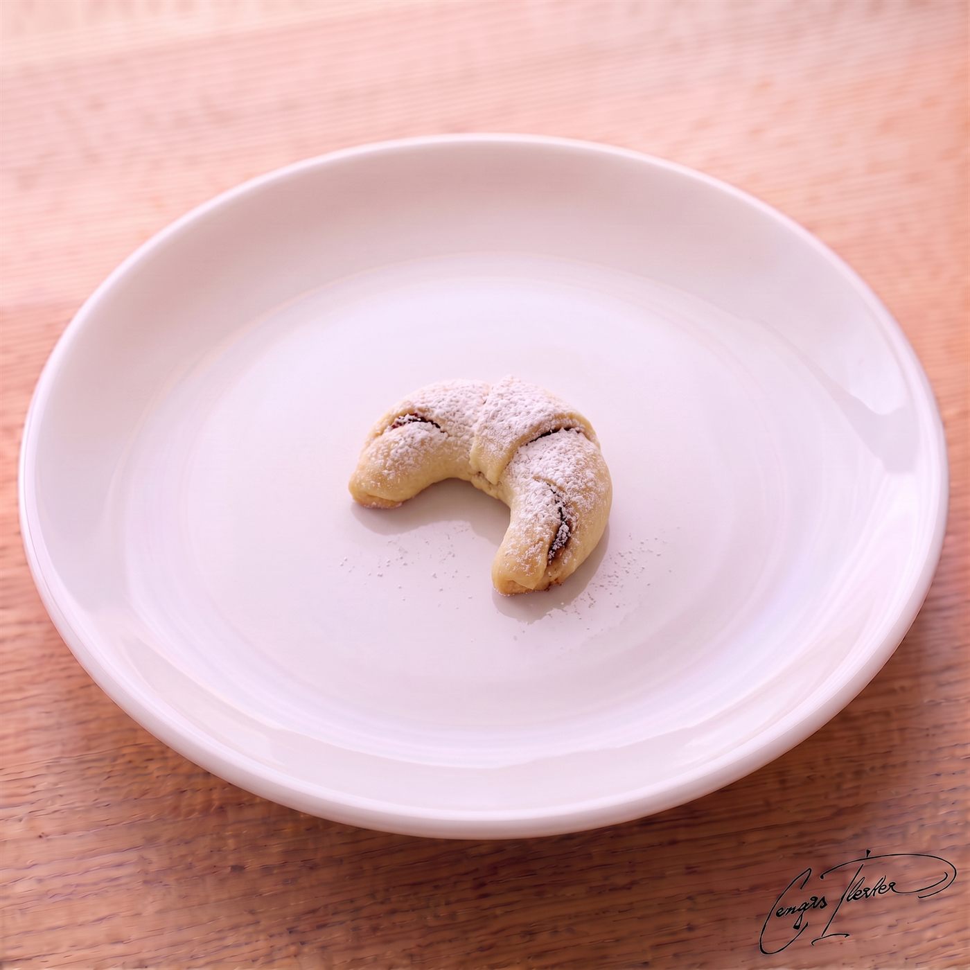 A single crescent-shaped elmalı kurabiye — a soft Turkish apple cookie dusted generously with powdered sugar — resting on a white plate.