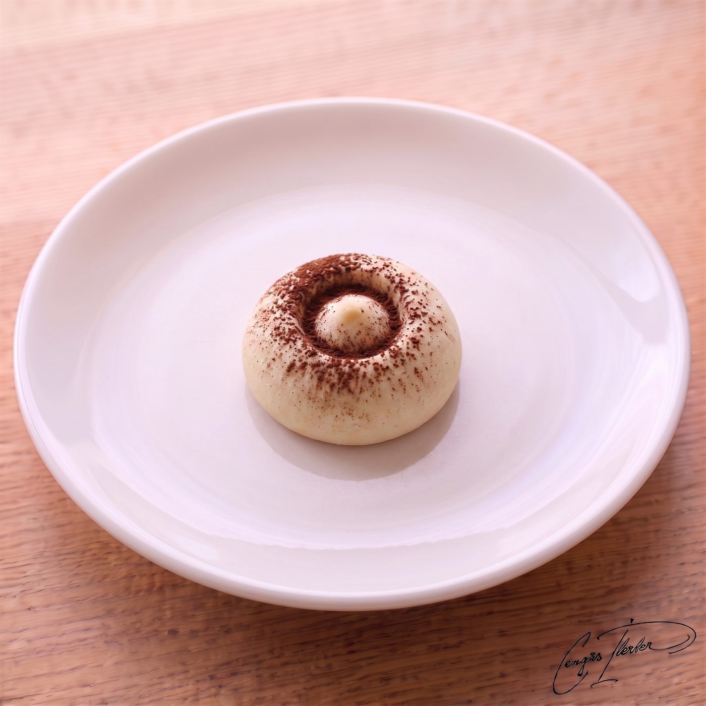 A single round, pale shortbread cookie on a white plate, with a cocoa-dusted center stamped to look exactly like a mushroom cap.
