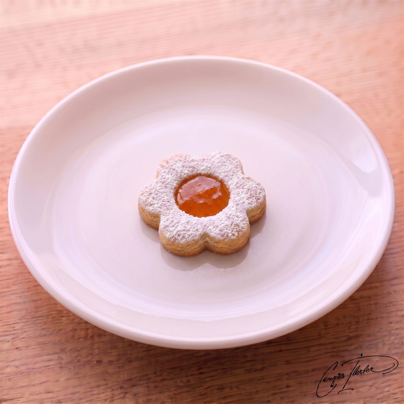 A single flower-shaped shortbread cookie dusted with powdered sugar, with a bright orange marmalade center, resting on a white plate.