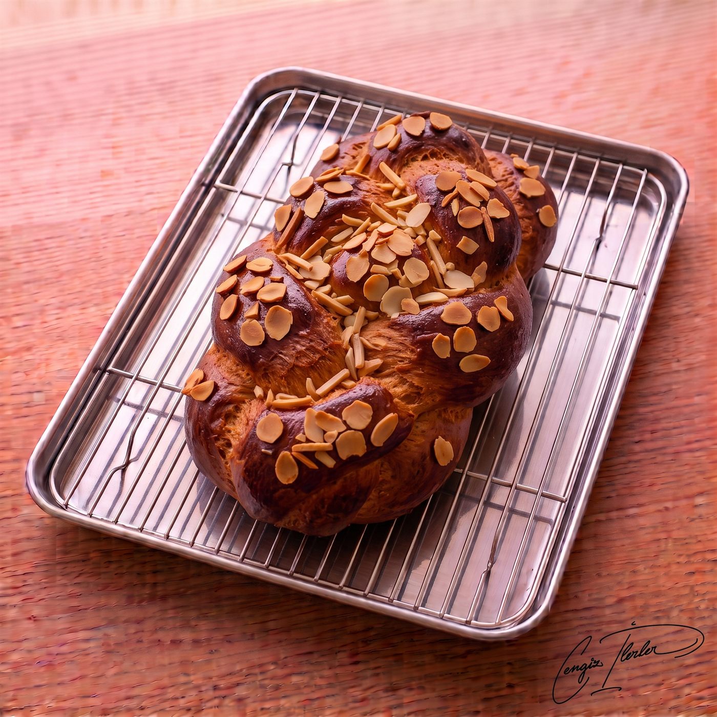A beautifully braided loaf of Paskalya Çöreği with a deeply browned, shiny crust, generously topped with sliced almonds, resting on a wire cooling rack.