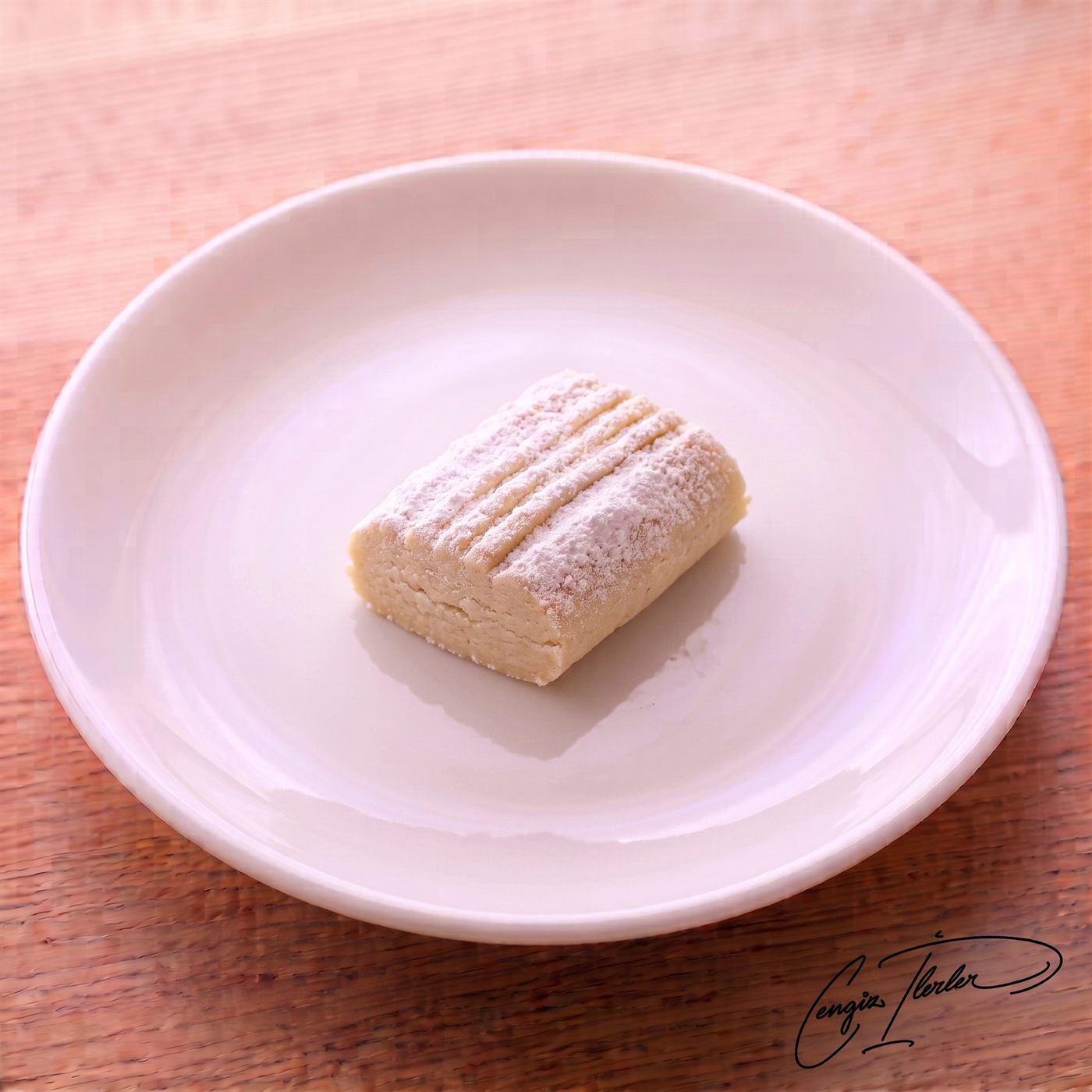 A single rectangular un kurabiyesi — a soft, crumbly Turkish flour cookie heavily dusted with powdered sugar, with traditional fork-pressed grooves along its top — resting on a white plate.