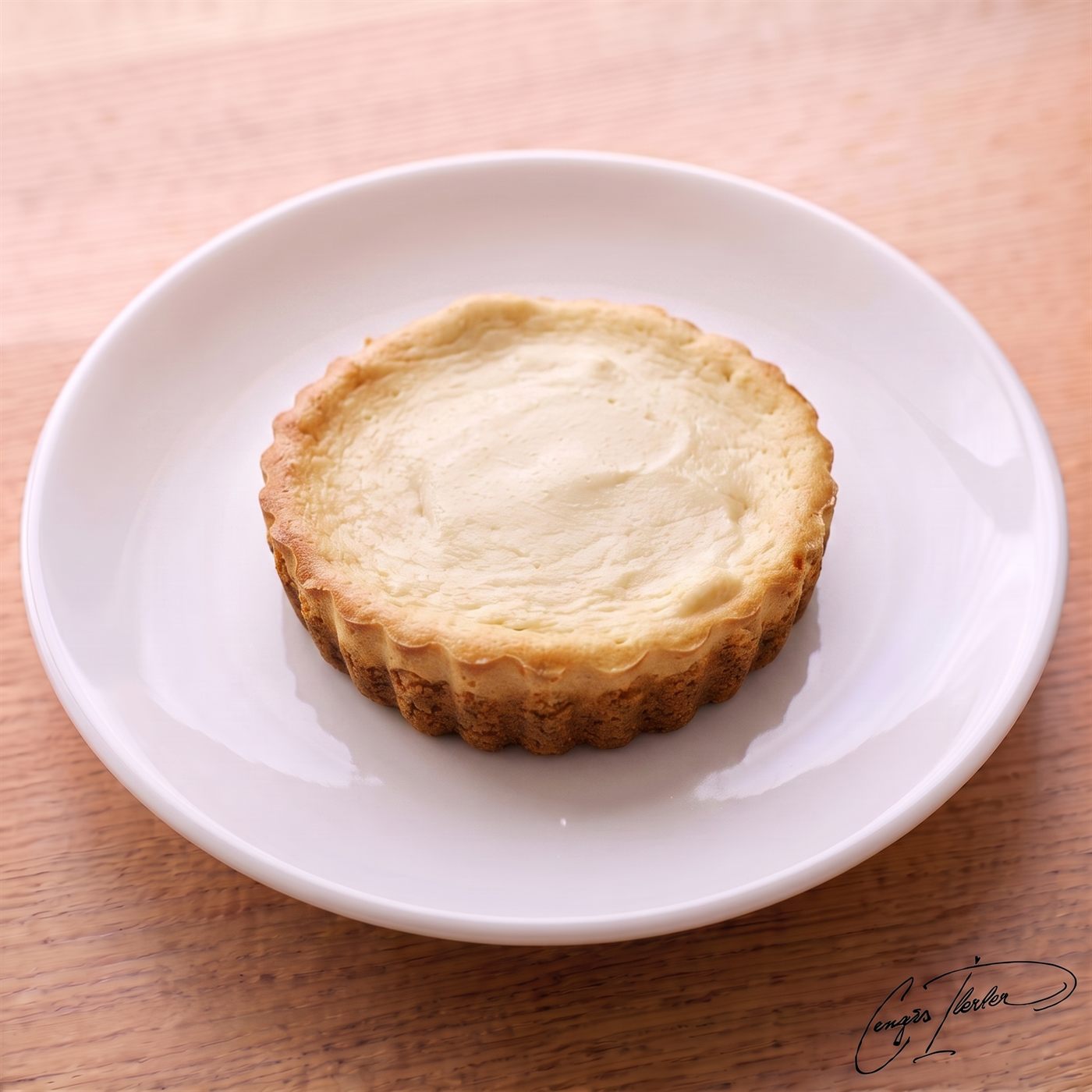 A round individual cheesecake with a golden fluted crust and a pale cream top, on a white plate on a wooden table.