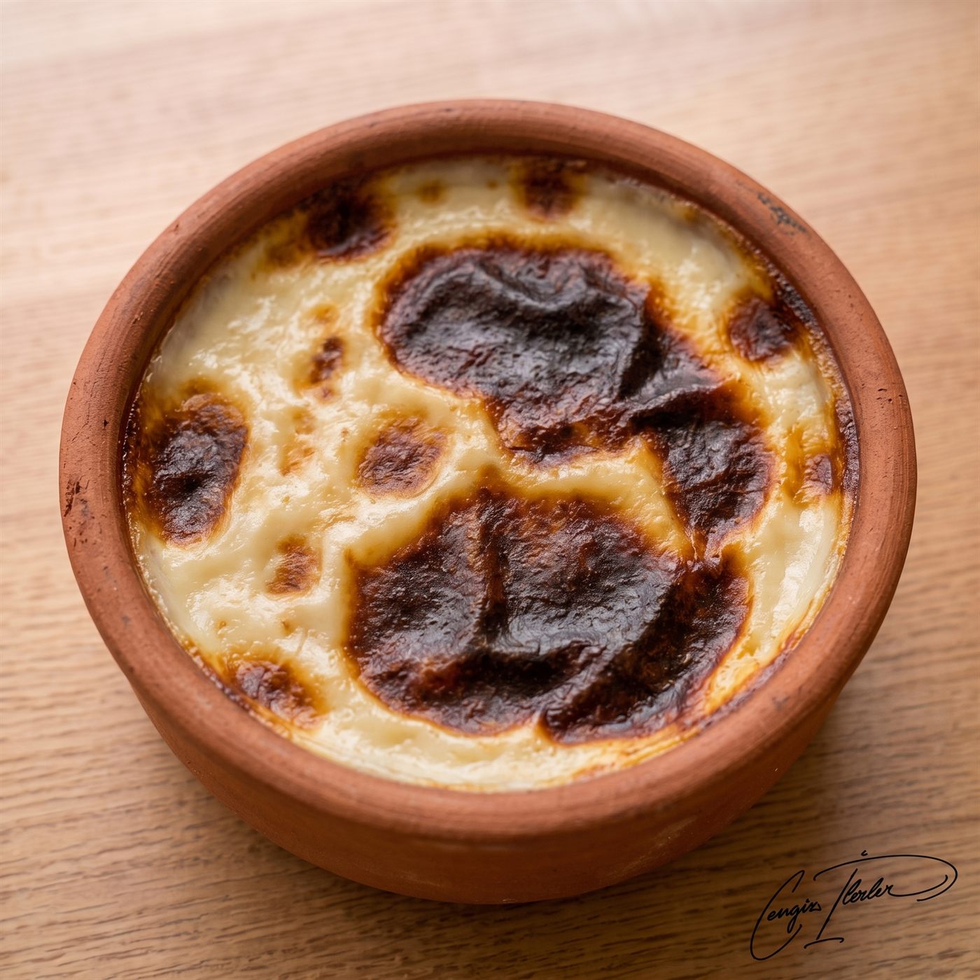 Fırın sütlaç in a clay bowl, top scorched deep brown, covered with crushed hazelnuts.
