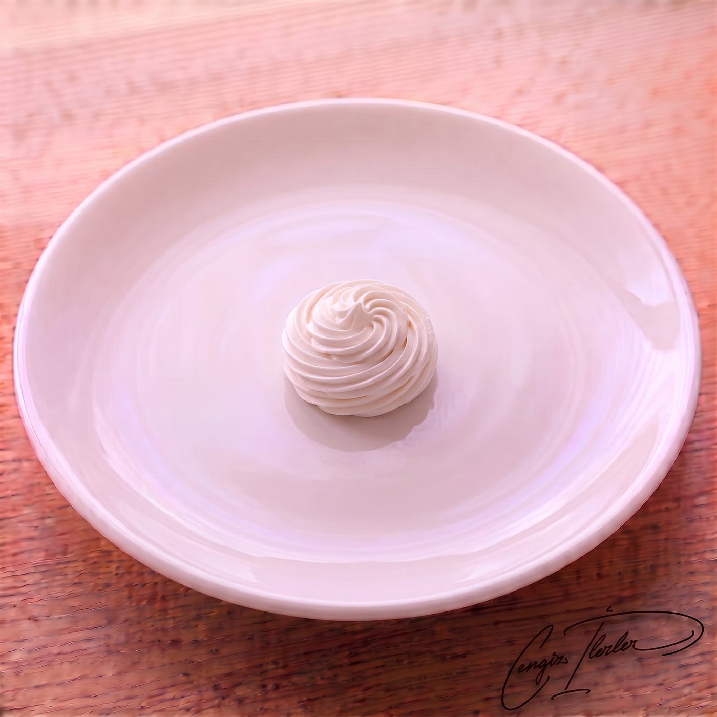 A single white meringue piped into a tall swirled spiral dome, on a white plate on a wooden table.